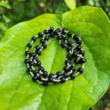 silver plated Karungali mala held in hand on leaf with tree background